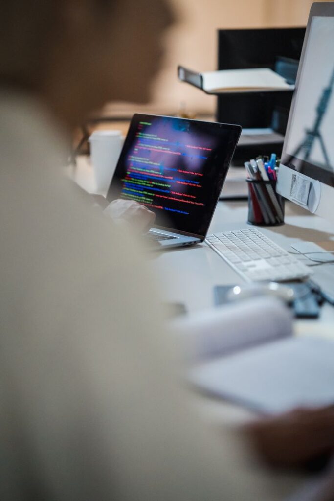 Mastering the First Impression: Your intriguing post title goes here Blurred figure at a desk with a laptop displaying colorful code, indicating a programming environment.